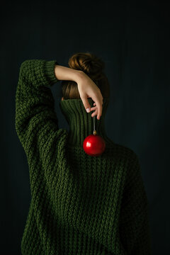 Conceptual portrait of a girl in a green sweater and a red christmas ball
