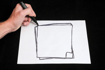 Closeup of a man drawing a rectangle on paper with a black marker