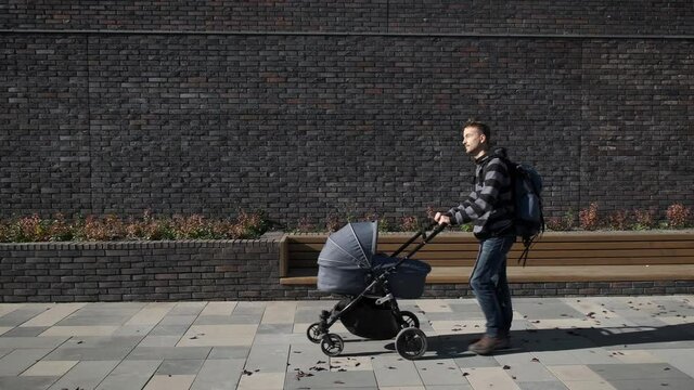 Father with newborn baby stroller walking on the city near brick wall. Man in maternity leave with pram.