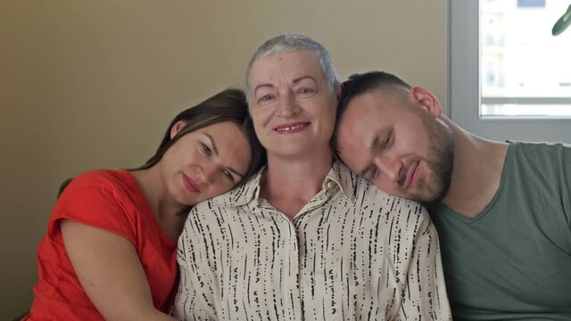 Family portrait. Adult son and daughter hug an elderly mother. Woman after chemotherapy and the children support the mother. Family values.