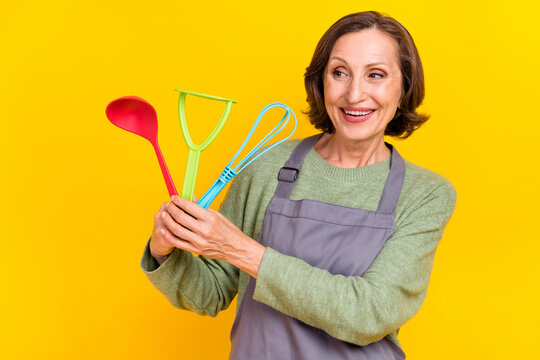 Portrait of attractive cheerful woman housewife holding spoon supplies homemade cuisine isolated over vivid yellow color background