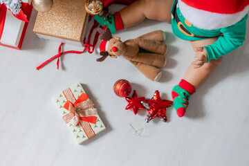 cute baby in a green bodysuit and a Santa hat decorates the Christmas tree with colorful balloons. child in a Christmas gnome costume. winter New Year's concept. space for text. top view