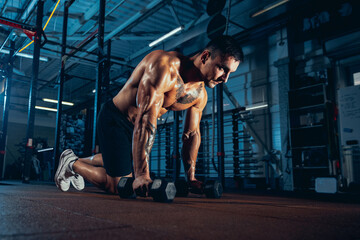 Portrait of muscled athlete, bodybuilder workouts alone at sport gym, indoors. Concept of sport, activity, healthy lifestyle