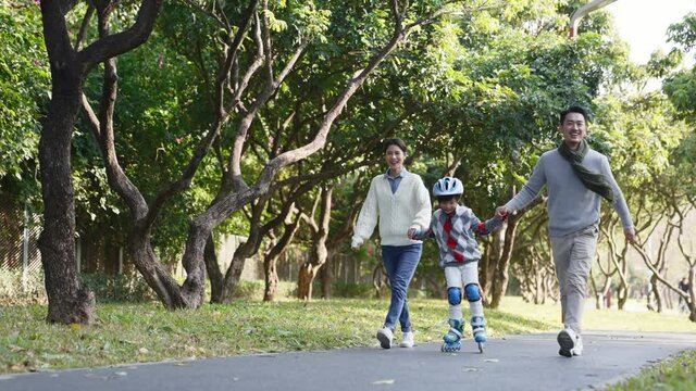 little asian boy learning roller skating outdoors in park with help from young parents