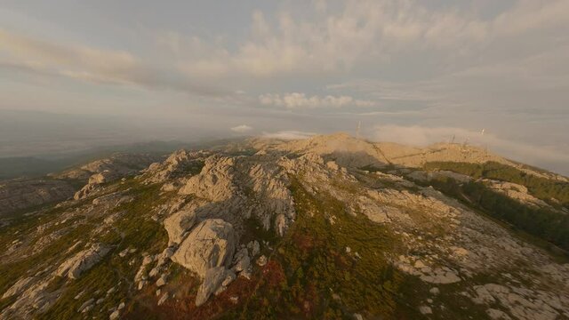 FPV video, mountain surfing, flying at high speed above the clouds with a granitic mountain range illuminated at sunrise. Mount Limbara (Monte Limbara) Tempio Pausania, Sardinia, Italy.
