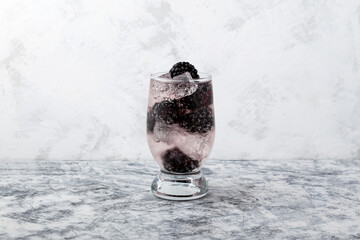 Soft fizzy drink with blackberry fruits. Iced summer drink. Refreshment Fruits lemonade made with soda water. Grey textured background, copy space