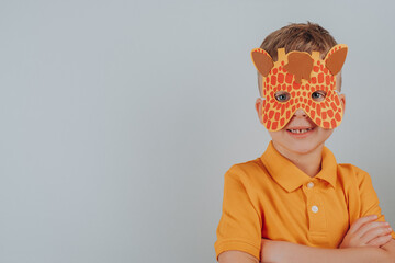 Smiling child with carnival giraffe mask isolated on gray background. School, kindergarten. Children's hands cut, glue, make. space for text
