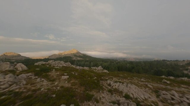 FPV video, mountain surfing, flying at high speed above the clouds with a granitic mountain range illuminated at sunrise. Mount Limbara (Monte Limbara) Tempio Pausania, Sardinia, Italy.