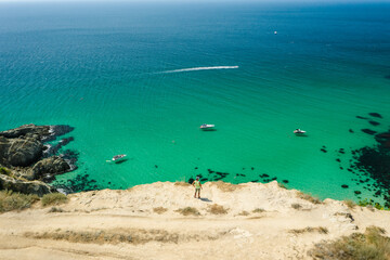 Obraz premium Man traveler on the edge in front of Bounty beach with crystal clear azure sea on a sunny day. Cape Fiolent in Sevastopol. Aerial view