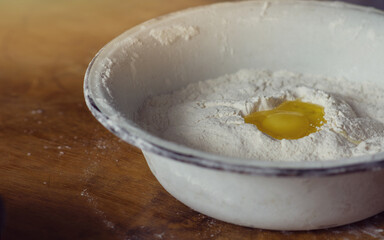 Broken raw egg in an enameled bowl with flour on a wooden table. Cooking concept, home cooking. Copy space