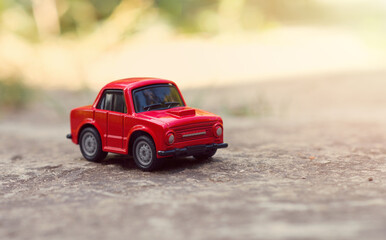 Model of a red toy car on the road outdoors. Close-up. Horizontal format. Selective focus. Copy space