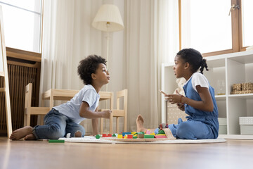 Happy friendly adorable small african american kids brother sister enjoying communicating, having fun playing toys, sitting on floor carpet in modern playroom, good siblings relations concept. - Powered by Adobe
