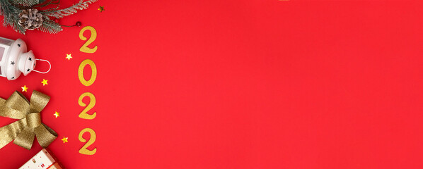 Happy New Year 2022. Golden numbers, golden and red Christmas toys, gifts, fir branches on a red background. the concept of a postcard with a top view and space to copy. Banner