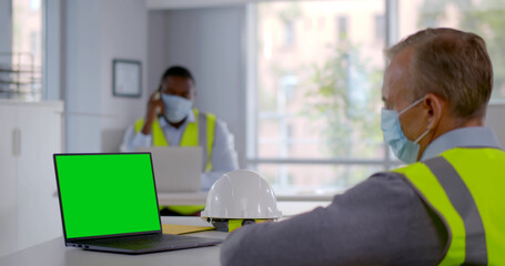 Side view of mature constructor in safety mask having video chat on laptop. Green screen