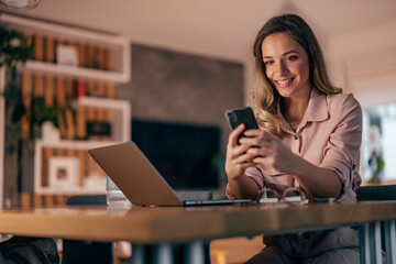 Smiling woman using smart phone while working at home office.