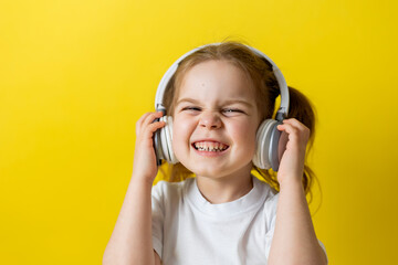 portrait of a cute cheerful little girl listening to music with white headphones. audiobooks, audio lessons. concept of education. photo studio, yellow background, text space. High quality photo