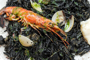 Close-up of delicious squid ink black noodles with king prawn on white plate. Traditional mediterranean seafood dish.