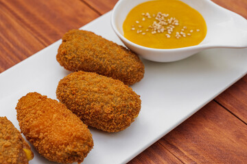 Fried croquettes with yellow sauce on white plate. Side view on wooden background.
