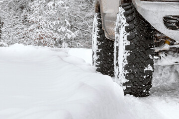 Off-road suv car wheel on snow in snowdrift against background of winter woods nature. Extreme winter, sports, travel, driving. Copy space