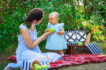 Mom with her newborn daughter at a picnic in the city park. The mother holds out a green apple to her daughter.