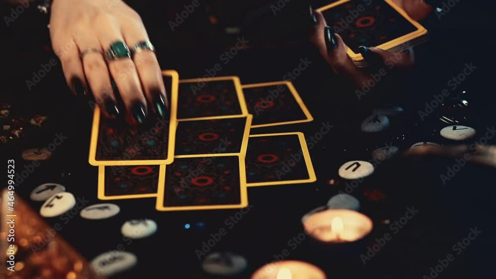 Sticker Divination and magic. The fortune teller lays out her Tarot cards and casts a spell over them. Close-up of hands with dark manicure and rings. A black table with scattered runes and a candle.