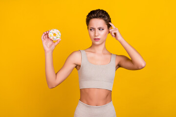 Photo of unsure doubtful lady hold doughnut decide diet wear grey top isolated yellow color background