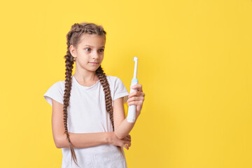 cute teenage girl with pigtails hairstyle holding an electric toothbrush in her hands on a yellow background