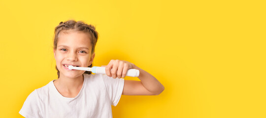 beautiful brown-haired teenager girl brushes her teeth with an electric toothbrush on a yellow background