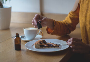 Fototapeta na wymiar A girl in a yellow jacket is having breakfast in a cafe. Women's hands add THC and CBD oil to cherry pie. The concept of using medical marijuana.