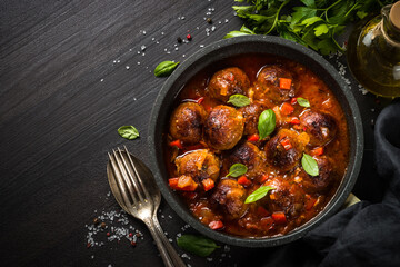 Meatballs in tomato sauce in black skillet on dark stone table. Top view copy space.