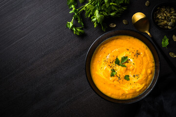 Pumpkin soup puree with cream. Top view image at black stone table.