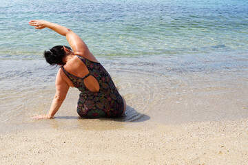 Fototapeta na wymiar lush woman performs yoga asana by the sea, outdoor exercise