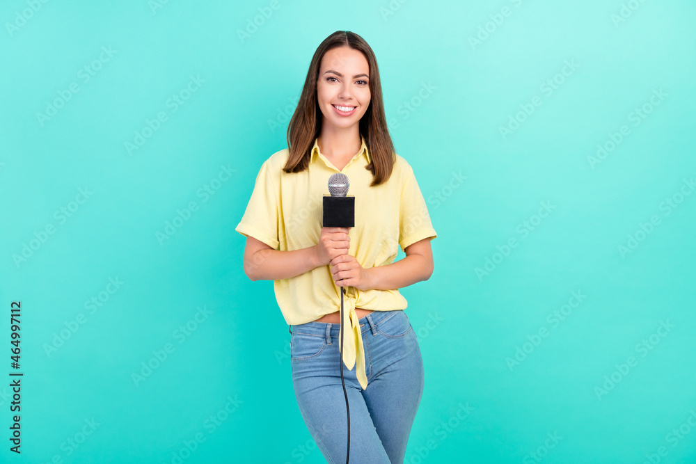 Poster photo of funny young brunette lady hold mic take interview wear yellow top jeans isolated on teal co