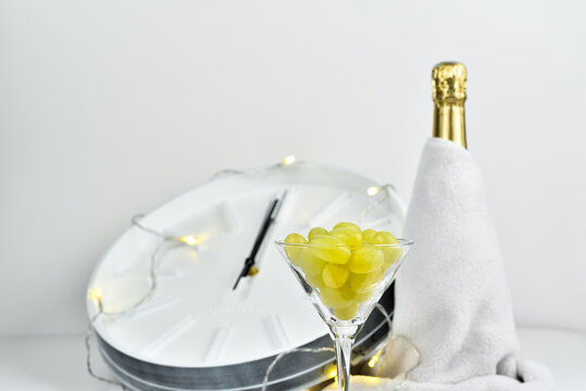 Glass with grapes on the background of a blurry clock and a bottle of champagne. Spanish tradition of eating twelve grapes to celebrate New Year.