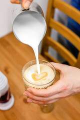 Women's and men's hands pour hot milk into a glass a coffee mug in a coffee shop
