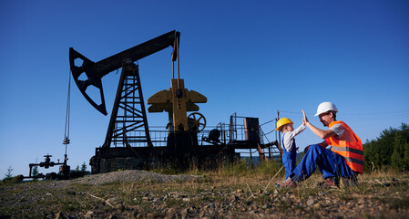 Male worker and cute child doing high five gesture while spending time in oil field with pump jack...