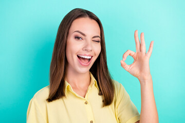 Photo of impressed millennial brunette lady show okey sign blink wear yellow blouse isolated on teal color background