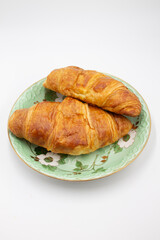 Two fresh juicy croissants with cheese, jam, cream on a green plate, a salad saucer with flowers, puff pastry on a white background