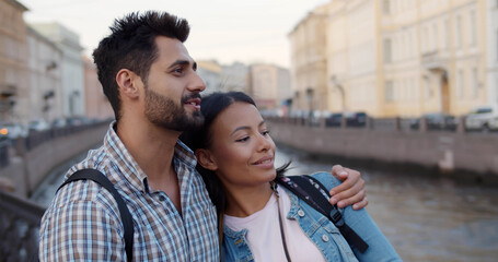 Multiethnic couple of tourists with backpack hug on city street - Powered by Adobe