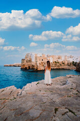Young girl in front of the village of Polignano a Mare, sky with white clouds