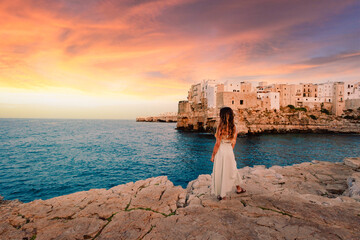 Young girl while watching the sunset in front of the village of Polignano a Mare