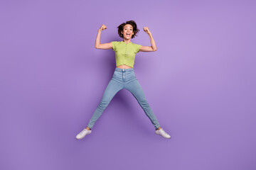 Fototapeta na wymiar Photo of attractive strong young woman dressed green t-shirt showing muscles jumping high isolated purple color background