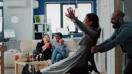 Workmates enjoying free time after work with office chair. Happy coworkers having fun with activity for entertainment and reaxation after hours. Colleagues enjoying leisure at party
