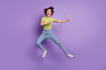 Fototapeta na wymiar Photo of strong funky young woman dressed green t-shirt practicing karate jumping high isolated purple color background