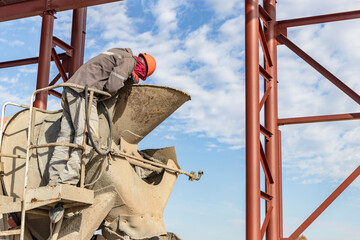A worker on a concrete mixer truck prepares to concrete a reinforced concrete structure. Equipment...