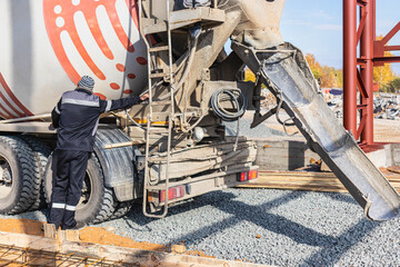 A worker on a concrete mixer truck prepares to concrete a reinforced concrete structure. Equipment...