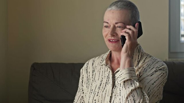 An elderly woman with very short hair after chemotherapy is talking on a cell phone.