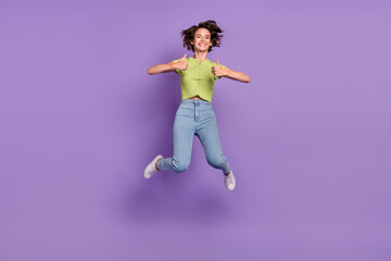 Fototapeta na wymiar Photo of excited pretty young lady wear green t-shirt smiling jumping showing thumbs up isolated violet color background