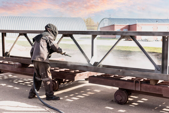 A worker in a special suit is sandblasting metal at an industrial site.