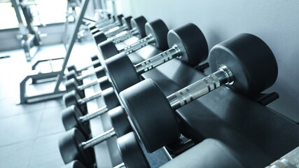 Obraz premium Black dumbbell set. Close a bunch of dumbbells on a rack in a monochromatic sports fitness center with natural light. Bodybuilding equipment concept with weights. Selective focus